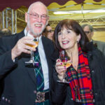 Festa di Natale 2014 Magazzino Allied International: Uomo in kilt e donna con sciarpa tartan sorridono con calici. MG_6935