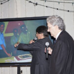 Festa di Natale 2015 Allied International: due uomini con microfoni presentano una foto di archivio.