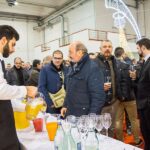 Festa di Natale 2016 Allied International: cameriere versa succo, persone socializzano. Atmosfera festosa al Magazzino.
