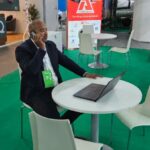 Uomo al NAPEC 2025 di Oran, Algeria, parla al telefono con laptop. Fiera petrolifera e del gas.