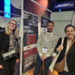 ftc25: Tre persone sorridono davanti a uno stand di tubi e raccordi Esope2.jpg.